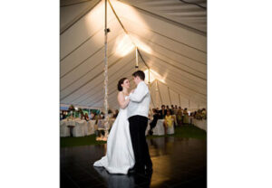 A bride and groom dancing under an all white event tent