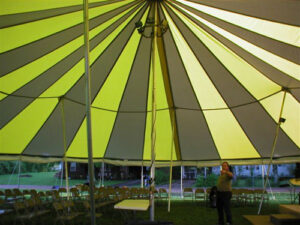 The underneath of a yellow and white pole tent being set up