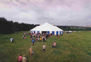 People going into a white pole tent with blue and white sidewall