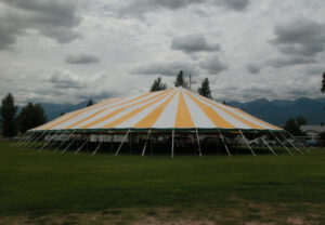 A large yellow and white pole tent set up in a field