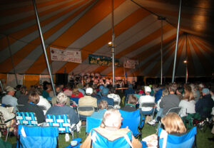 Large group of people gathered under a yellow and white pole tent