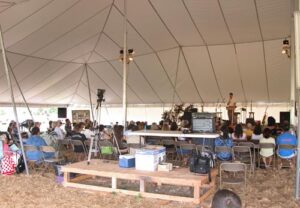 Under an all white tent with a stage and chairs set up inside