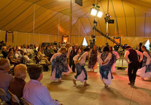 A group of people dancing under an all yellow pole tent