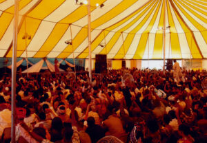 People worshipping under a large yellow and white revival tent