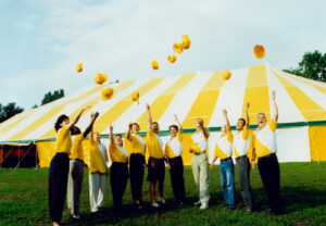 A group of people throwing their caps in matching shirts in front of a yellow and white tent