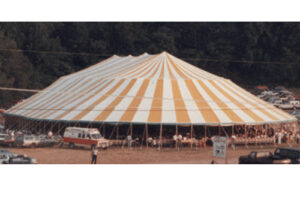 Large yellow and white pole tent with people gathered inside